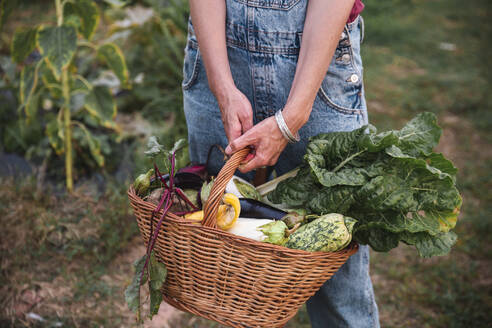 Frau hält Weidenkorb mit Gemüse im Obstgarten - PCLF00807