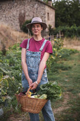 Lächelnde Frau hält Weidenkorb mit Gemüse im Obstgarten - PCLF00808