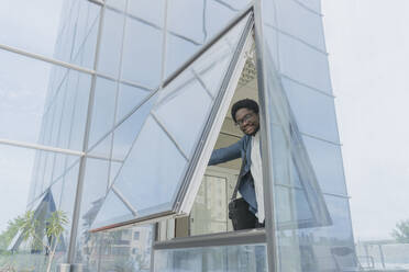 Smiling businessman opening window of office building - OSF02286