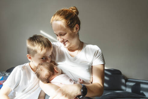 Mutter, die ihre neugeborene Tochter in der Nähe ihres Sohnes zu Hause stillt - IHF01759