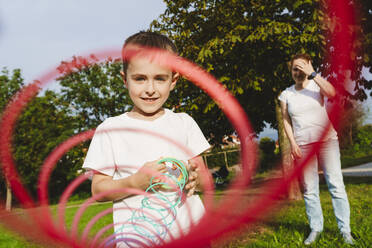 Junge hält Frühlingsspielzeug mit Mutter im Hintergrund im Park - IHF01764