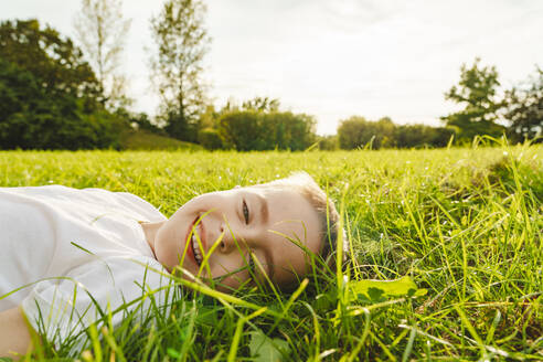 Lächelnder Junge auf Gras im Park liegend - IHF01766