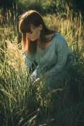 Young redhead woman kneeling in meadow - ADF00187