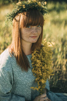 Young redhead woman wearing wreath of flowers in field - ADF00188