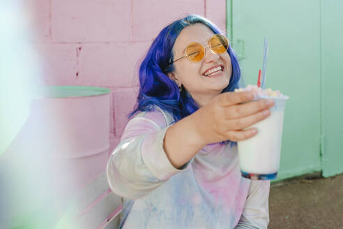 Glückliche Frau mit gefärbten Haaren hält ein Getränk in einem Café - YTF01235