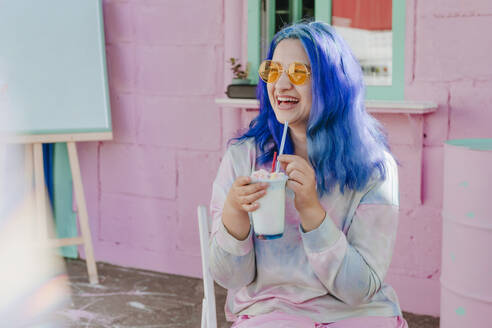 Glückliche Frau mit gefärbten blauen Haaren hält ein Getränk in einem Cafe - YTF01236