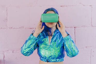 Frau mit gefärbtem Haar, die einen Virtual-Reality-Simulator vor einer rosa Wand trägt - YTF01243