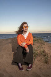 Thoughtful woman sitting on sand at beach - VPIF08893