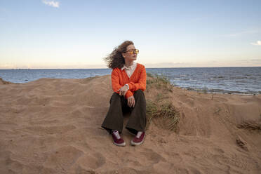 Kontemplative junge Frau sitzt am Strand im Sand - VPIF08895