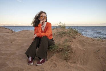 Frau sitzend mit Hand am Kinn am Strand - VPIF08897