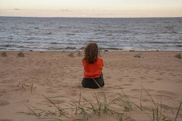 Woman sitting on sand in front of sea at beach - VPIF08901