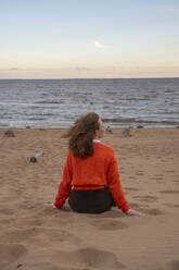 Junge Frau sitzt auf Sand vor dem Meer am Strand - VPIF08902