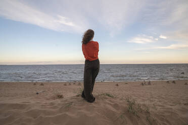 Frau steht auf Sand vor dem Meer unter bewölktem Himmel - VPIF08903