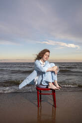 Woman sitting on chair in front of sea at sunset - VPIF08905