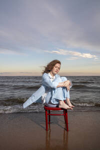 Frau sitzt auf einem Stuhl vor dem Meer bei Sonnenuntergang - VPIF08905