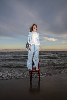 Young woman standing on chair at beach - VPIF08906