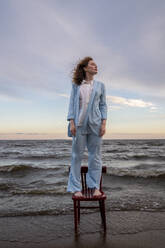 Young woman standing on chair in front of sea - VPIF08907