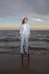 Woman standing on chair at beach - VPIF08910