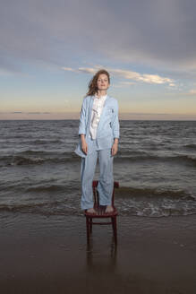 Woman standing on chair at beach - VPIF08910