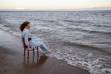 Junge Frau sitzt auf einem Stuhl im Meerwasser am Strand - VPIF08912