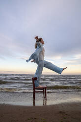 Frau steht und balanciert auf einem Stuhl am Strand - VPIF08913