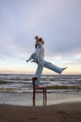 Woman standing and balancing on chair at beach - VPIF08913