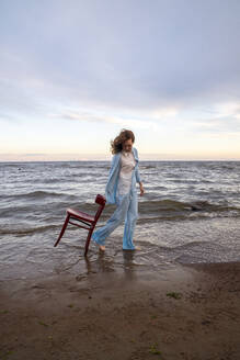 Frau geht mit Stuhl am Strand spazieren - VPIF08914