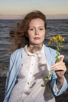 Junge Frau hält gelbe Blumen am Strand - VPIF08916