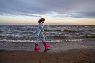 Junge Frau mit rosa Gummistiefeln und Spaziergang am Strand - VPIF08923