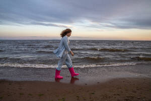 Junge Frau mit rosa Gummistiefeln und Spaziergang am Strand - VPIF08923