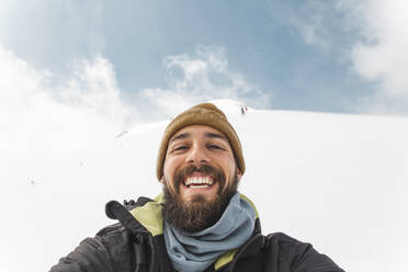 Happy man wearing knit hat taking selfie in snow - PCLF00849