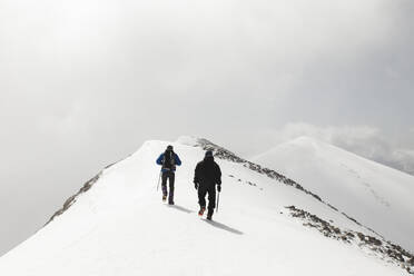 Männer wandern mit Stock auf einem verschneiten Berg - PCLF00850
