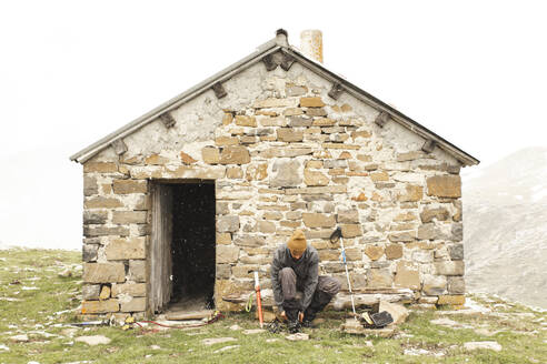 Man tying shoe near brick house on mountain - PCLF00855