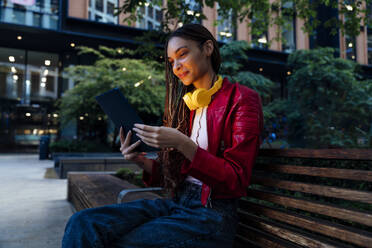 Lächelnde junge Frau mit Tablet-PC auf einer Bank - OIPF03524