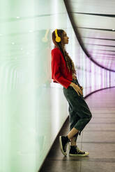 Junge Frau hört Musik über Kopfhörer und lehnt sich an eine Wand in einem U-Bahn-Tunnel - OIPF03531