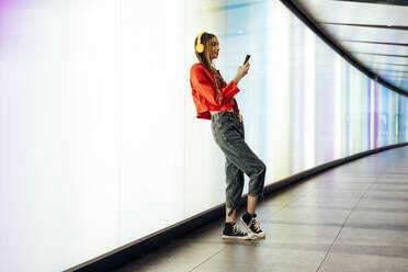 Junge Frau hört Musik und benutzt ein Smartphone in einem beleuchteten U-Bahn-Tunnel - OIPF03533