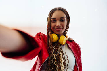 Smiling woman with braided hair taking selfie in front of white wall - OIPF03534