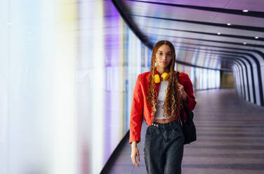 Confident woman with backpack walking in illuminated underground tunnel - OIPF03557