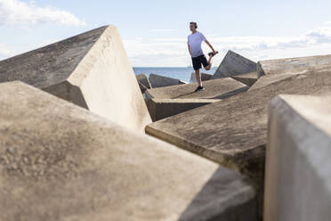 Man stretching legs on rocks near sea - MMPF00981