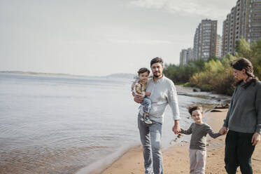 Glückliche Familie beim gemeinsamen Spaziergang am Strand - ANAF02234