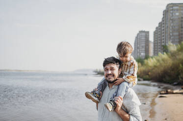 Smiling father carrying son on shoulders at beach - ANAF02238