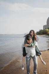 Mann nimmt Frau am Strand huckepack - ANAF02240