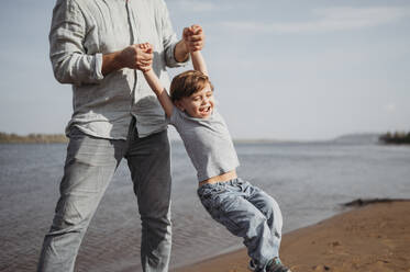 Vater hält Hände und spielt mit Sohn am Strand - ANAF02243