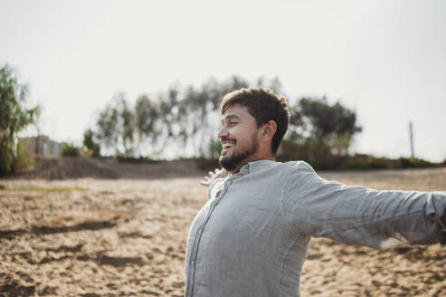 Happy man standing with arms outstretched at beach - ANAF02246