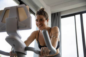 Lächelnde Frau, die auf dem Fahrrad trainiert und einen Tablet-PC im heimischen Wohnzimmer benutzt - IKF01396