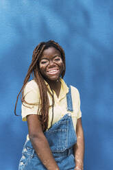 Glückliche junge Frau mit Vitiligo vor einer blauen Wand - PNAF06043