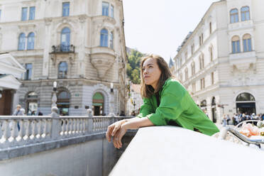 Contemplative woman leaning on bridge in city - NDEF01180