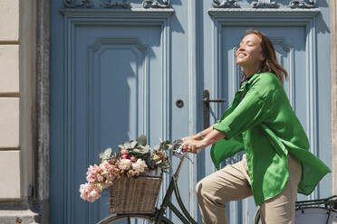 Lächelnde Frau auf dem Fahrrad vor der Tür an einem sonnigen Tag - NDEF01188