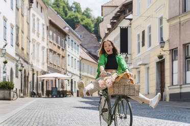 Fröhliche Frau auf dem Fahrrad auf der Straße in der Stadt - NDEF01198