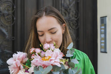 Woman smelling flowers in front of door - NDEF01213